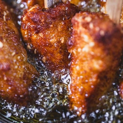 macrofotografía de pollo apanizado en colador con aceite para freír