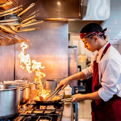 hombre en cocina profesional sellando carne en una sartén con aceite para freír mientras sale fuego