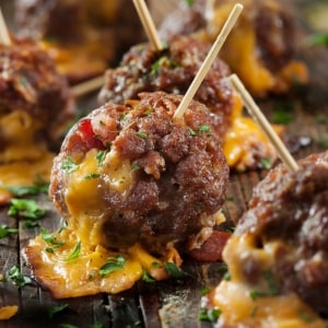 Albóndigas de carne de res y cerdo rellenas con queso cheddar fundido, que cae sobre la bandeja. Las albóndigas tienen pinchos y perejil picado por arriba.