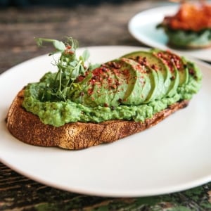 Pan de masa madre tostado con aguacate machacado y aguacate en tajadas encima, decorado con microgreens y ají molido.