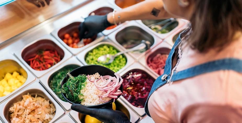 cocinera en línea de ensamblaje para armar un bowl con arroz, cebolla morada, verdes, entre otros ingredientes