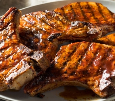 Chuletas de cerdo con salsa barbacoa, cocidas en la parrilla y servidas en un plato blanco.
