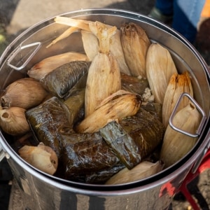 Variedad de tamales en hojas de maíz y plátano cocinándose al vapor en una olla doble de acero inoxidable.