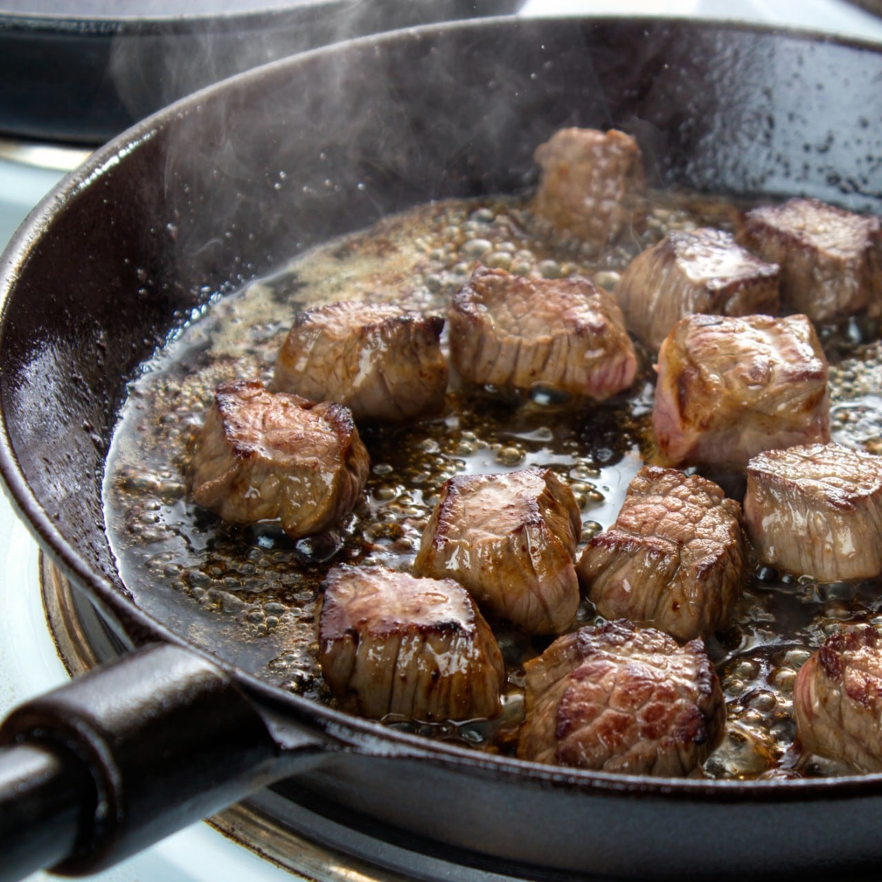 Frying beef bottom round roast cubes in cast iron skillet , meat flipped once