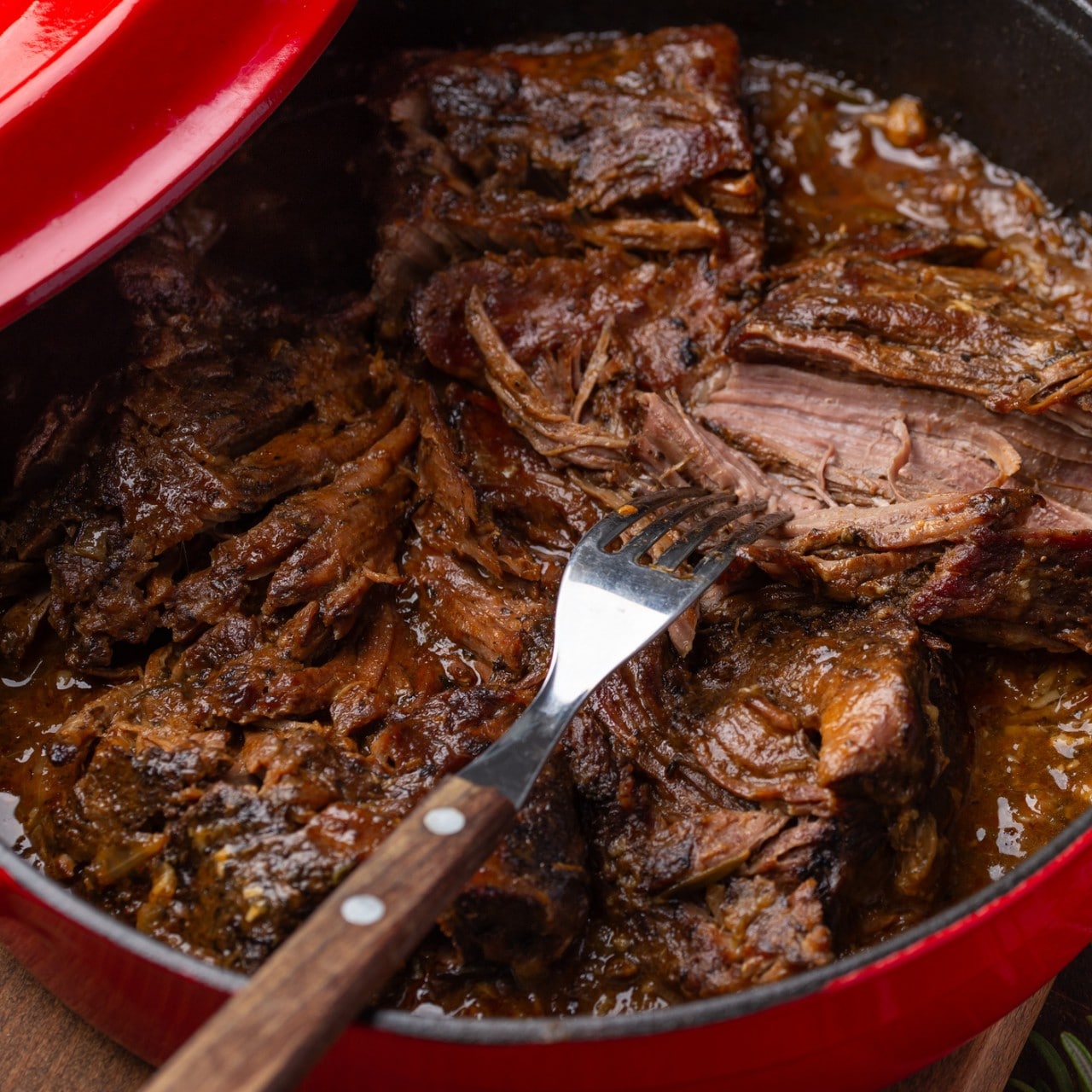 braised beef, slow cooked meat stew in cast iron cooking pot, wooden background