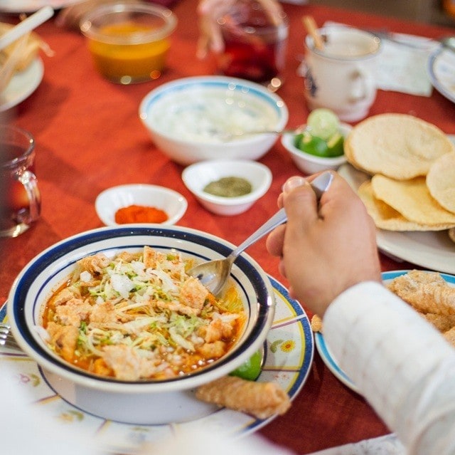 Hombre comiendo sopa de tortilla servida en un plato hondo. En la mesa también hay platos con tortillas, arroz blanco, limón verde y salsas. Hombre comiendo sopa de tortilla servida en un plato hondo. En la mesa también hay platos con tortillas, arroz blanco, limón verde y salsas.