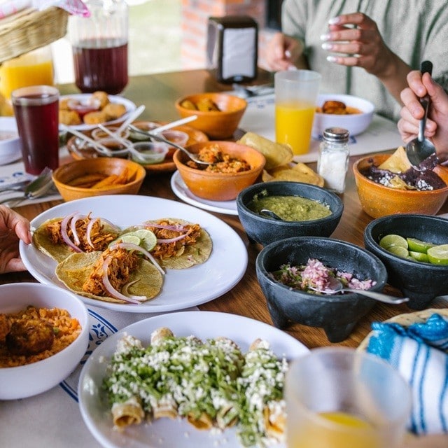 Grupo de amigos compartiendo una comida en un restaurante. Entre los platillos hay tacos de tinga de pollo, arroz rojo, tacos dorados, frijoles y guacamole. También aguas frescas y jugos. Grupo de amigos compartiendo una comida en un restaurante. Entre los platillos hay tacos de tinga de pollo, arroz rojo, tacos dorados, frijoles y guacamole. También aguas frescas y jugos.