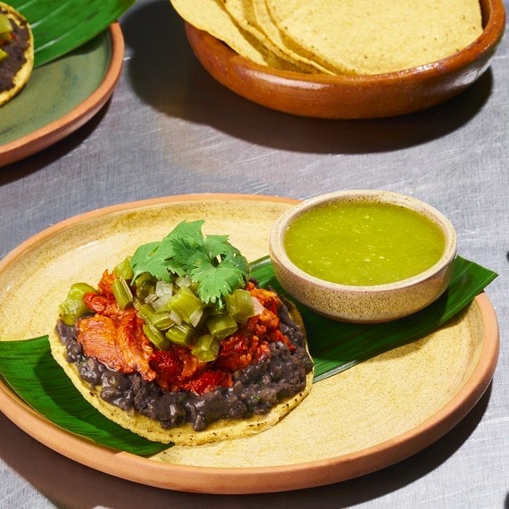 Tostada de cochinita con nopales emplatada para servir en un restaurante, con salsa verde al lado. Tostada de cochinita con nopales emplatada para servir en un restaurante, con salsa verde al lado.