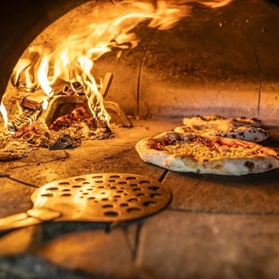 Traditional oven for baking pizza with burning wood and shovel. The cook rotates the pizza in the oven to ensure even baking.