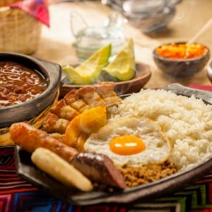 Bandeja paisa, platillo típico de comida colombiana, compuesto de carne molida, chorizo, huevo frito, chicharrón, arepa y arroz blanco, acompañada por frijoles, rebanadas de aguacate y salsa roja.