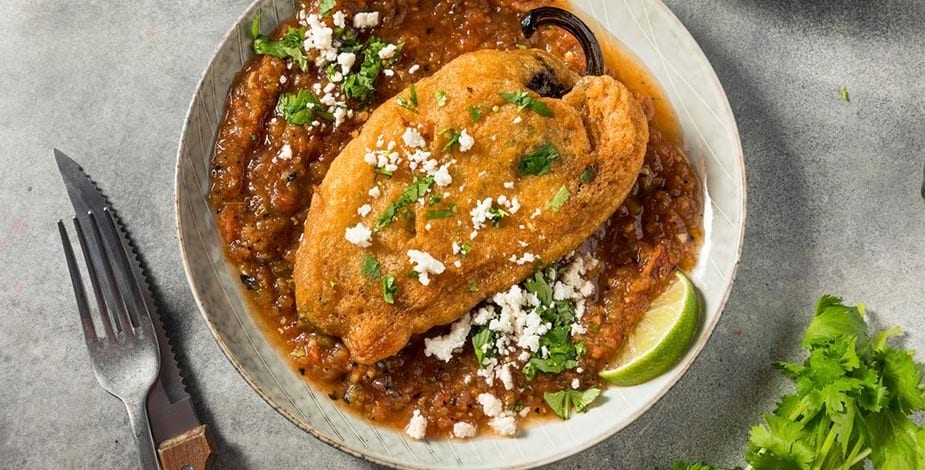 chile relleno con queso sobre salsa con cilantro y lima, en plato de cerámica blanco