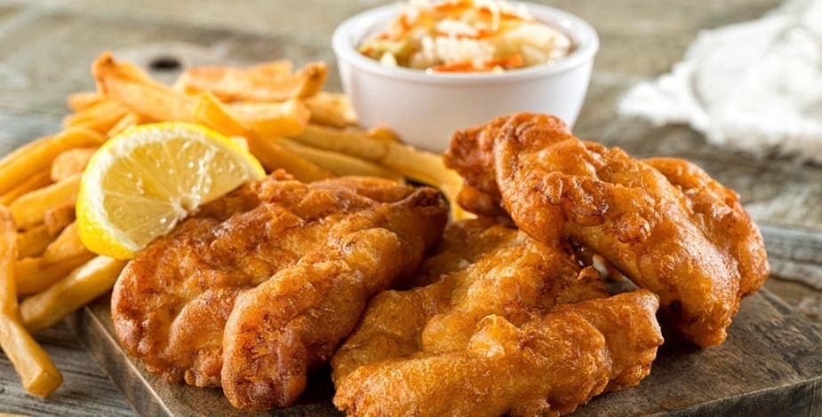 pescados fritos con limón, papas fritas y salsa en un bol aparte, sobre tabla de madera