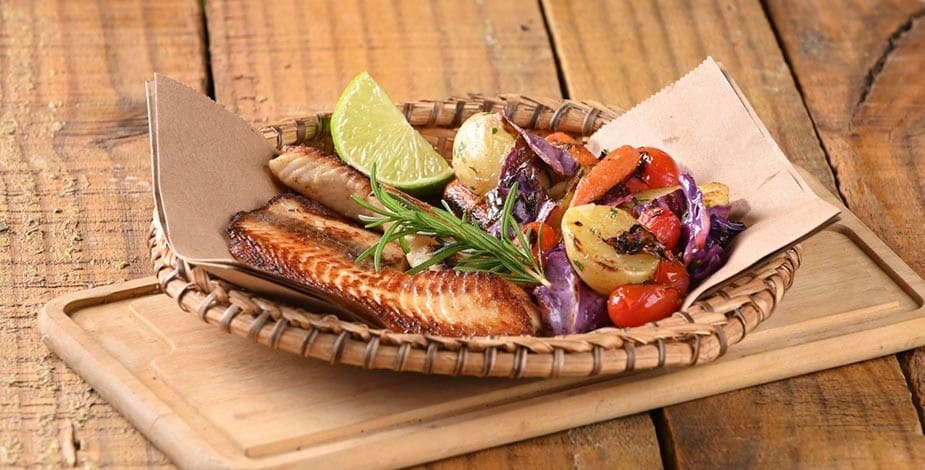 tilapia, pescado frito con vegetales asados, lima y romero servido en una canasta sobre una tabla de madera