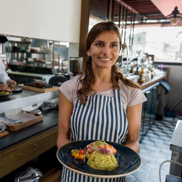 Una mujer sonriente, que trabaja en un restaurante, está sirviendo un plato de comida saludable. Una mujer sonriente, que trabaja en un restaurante, está sirviendo un plato de comida saludable.