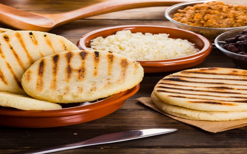 Arepas venezolanas servidas en una fuente y sobre un papel de estraza, acompañadas por rellenos y acompañamientos, como arroz blanco, frijoles negros y un guisado. Arepas venezolanas servidas en una fuente y sobre un papel de estraza, acompañadas por rellenos y acompañamientos, como arroz blanco, frijoles negros y un guisado.
