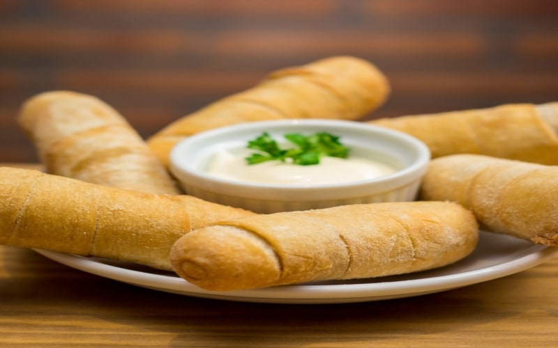 Plato de tequeños servidos junto a una salsa de queso con hierbas, sobre mesa de madera. Plato de tequeños servidos junto a una salsa de queso con hierbas, sobre mesa de madera.
