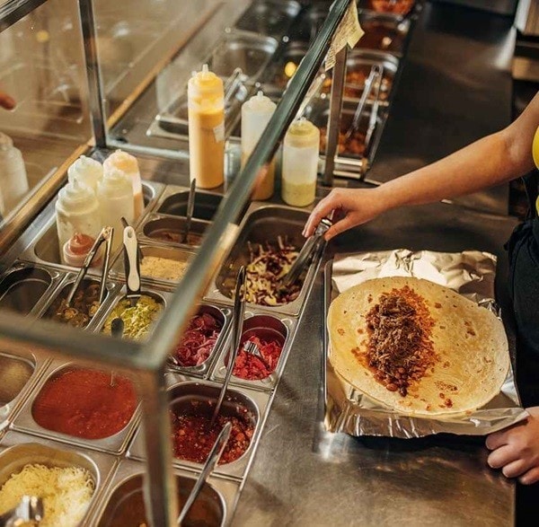 Detalle de tacos abiertos siendo llenados cuidadosamente con porciones exactas Detalle de tacos abiertos siendo llenados cuidadosamente con porciones exactas