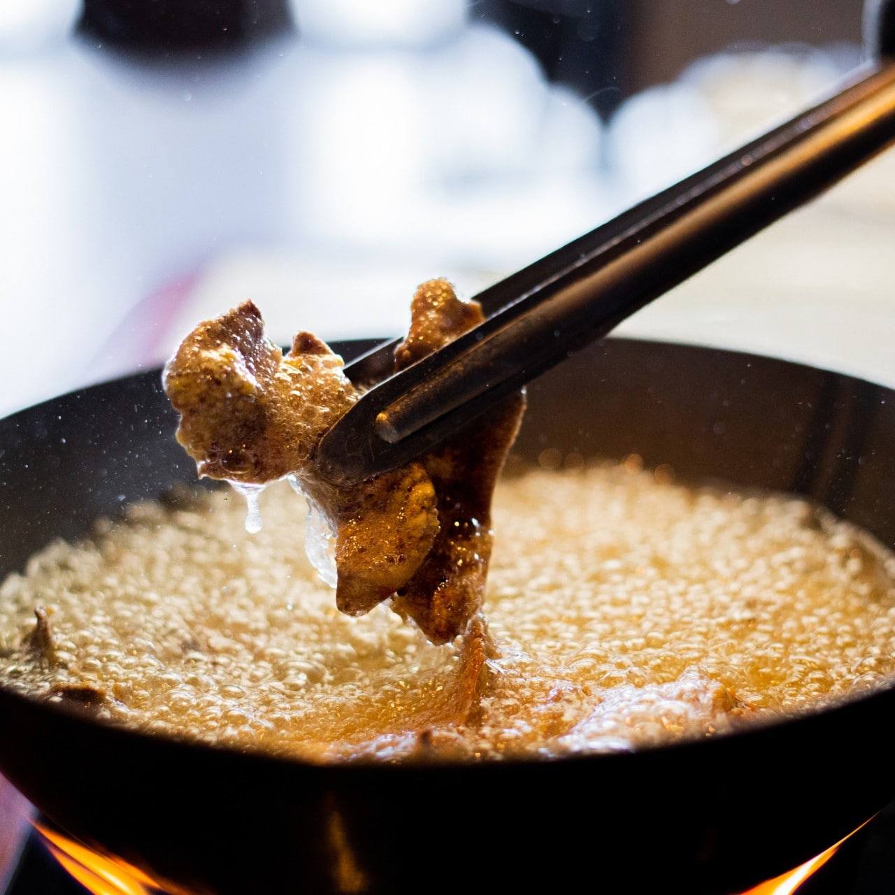 Pieces of meat fried in hot oil are removed from the pan with the help of tongs.