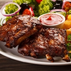 Costillas de cerdo con salsa BBQ servidas en un plato con salsa extra, papas a la francesa onduladas y ensalada de lechuga, cebolla, rábano, aceitunas negras y jitomate. Costillas de cerdo con salsa BBQ servidas en un plato con salsa extra, papas a la francesa onduladas y ensalada de lechuga, cebolla, rábano, aceitunas negras y jitomate.