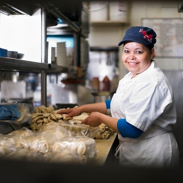 Una cocinera sonriente coloca tamales en una bolsa para conservarlos mejor.