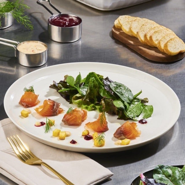 Plato con pescado curado, ensalada de hojas verdes, pequeños cubos de plátano y hojas de eneldo. Plato con pescado curado, ensalada de hojas verdes, pequeños cubos de plátano y hojas de eneldo.
