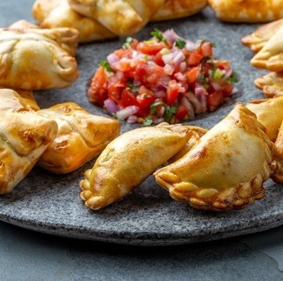Different little cocktail EMPANADAS on stone plate with tomato sauce and guacamole . Gray background. Latin American and Spanish tipical food.
