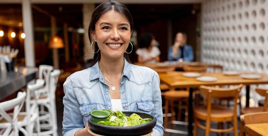 mujer latina sonriente en restaurante sosteniendo un bowl de ensalada con aderezo