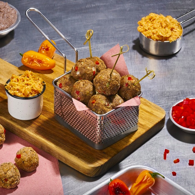 Canasta metálica con albóndigas de frijol, apoyada sobre una tabla y acompañada por un ramekin con kimchi y pimientos anaranjados. Además, sobre la mesada de acero inoxidable hay otros ingredientes y preparaciones. Canasta metálica con albóndigas de frijol, apoyada sobre una tabla y acompañada por un ramekin con kimchi y pimientos anaranjados. Además, sobre la mesada de acero inoxidable hay otros ingredientes y preparaciones.