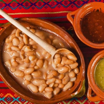 Sopa de frijoles guisados servida en una fuente de barro junto a ollitas con salsa roja y salsa verde, todo apoyado sobre un mantel tradicional. Sopa de frijoles guisados servida en una fuente de barro junto a ollitas con salsa roja y salsa verde, todo apoyado sobre un mantel tradicional.