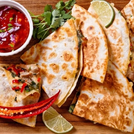 quesadillas mexicanas con pollo, cebollín, chile, hojas de cilantro servidas con salsa de tomate y lima sobre tabla de madera