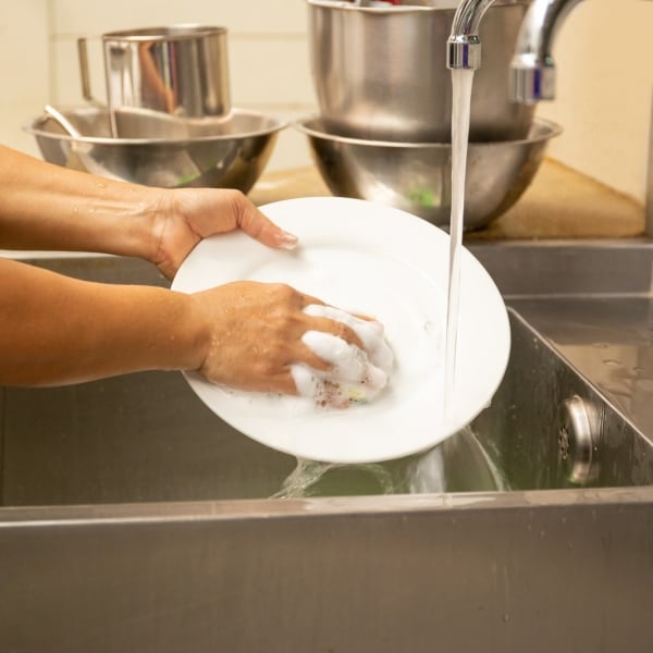 Hands washing dirty dishes with running water in kitchen sink