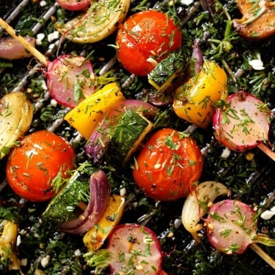 Brochetas de verduras asándose a la parrilla. Entre ellas hay rábano, tomate cereza, calabacita, cebolla morada y pimiento amarillo, aderezadas con una mezcla de hierbas. Brochetas de verduras asándose a la parrilla. Entre ellas hay rábano, tomate cereza, calabacita, cebolla morada y pimiento amarillo, aderezadas con una mezcla de hierbas.