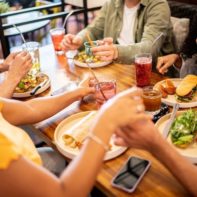 Grupo de adolescentes come en un restaurante. En la mesa hay platos con sandwiches, wraps y tostadas con guarniciones y aderezos. Grupo de adolescentes come en un restaurante. En la mesa hay platos con sandwiches, wraps y tostadas con guarniciones y aderezos.