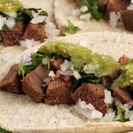 tacos de lengua de res con cebolla, guacamole y hojas de cilantro