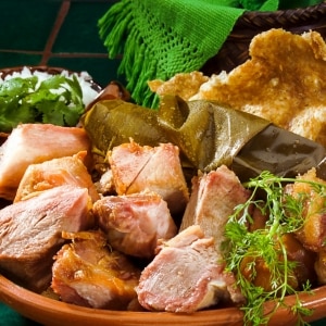 Carnitas calientes, platillo típico mexicano con trozos de carne de cerdo confitada servida con hoja de plátano, chicharrón y hierbas servido en una cazuela de barro.