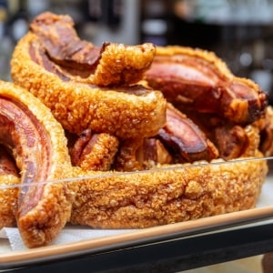 Bandeja de chicharrones carnudos, al estilo de los torreznos españoles, con la piel dorada y crocante y la carne roja, exhibidos en la vitrina de un negocio de comidas.