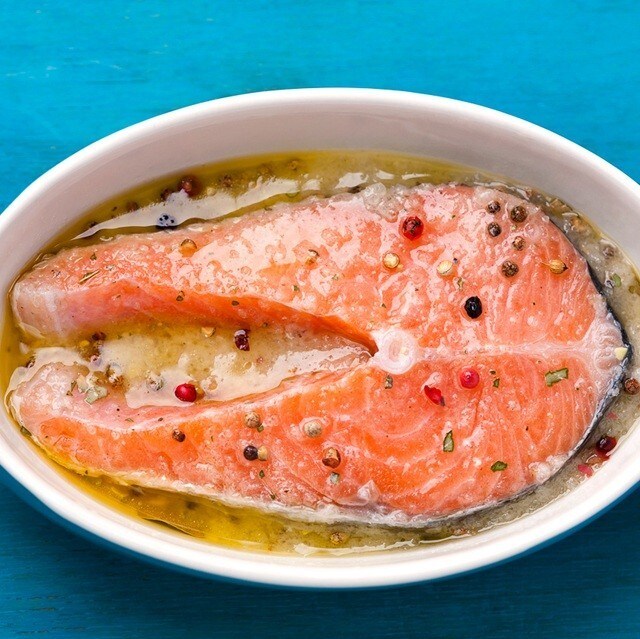 Rodaja de salmón rosado colocado en una fuente con una marinada a base de aceite, limón y granos de pimienta. Rodaja de salmón rosado colocado en una fuente con una marinada a base de aceite, limón y granos de pimienta.