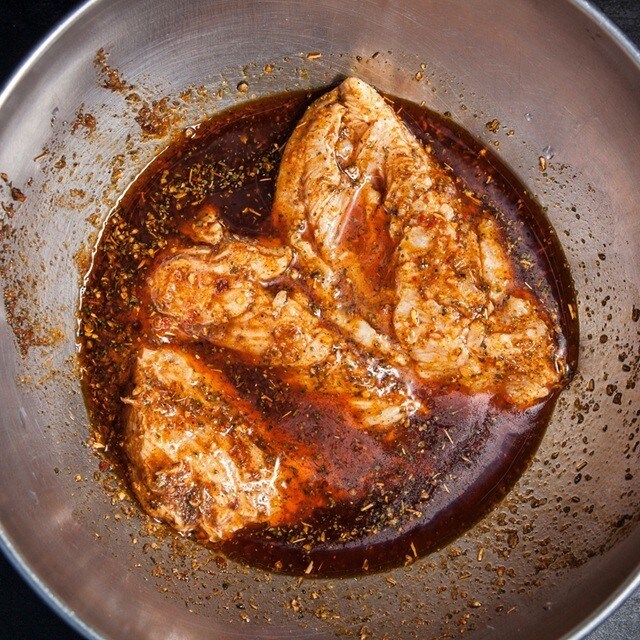 pechugas de pollo en un bol metálico sumergidas en un líquido para marinar a base de salsa de soja y hierbas. pechugas de pollo en un bol metálico sumergidas en un líquido para marinar a base de salsa de soja y hierbas.