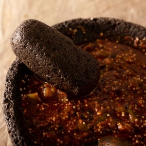 Salsa roja hecha con chiles rojos, cebolla y jitomate martajados en el molcajete. Se ven pequeños trozos y semillas de los ingredientes.