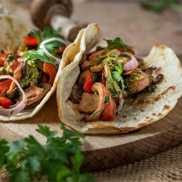 tacos veganos de setas, tomates, cebolla y perejil, sobre tabla de madera