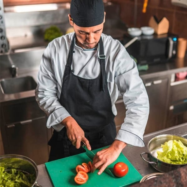 cocinero cortando tomates sobre tabla de cortar verde en cocina profesional