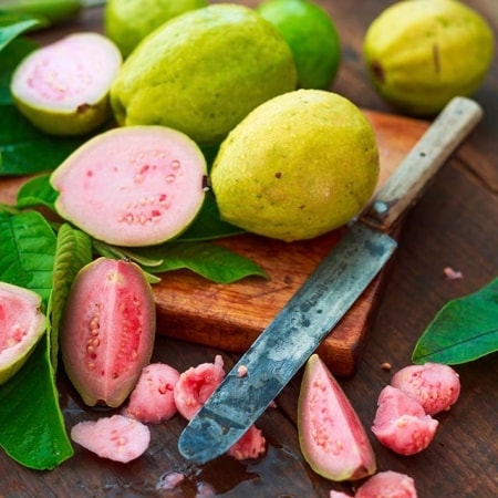guayabas enteras y cortadas con hojas sobre tabla de madera y cuchillo largo