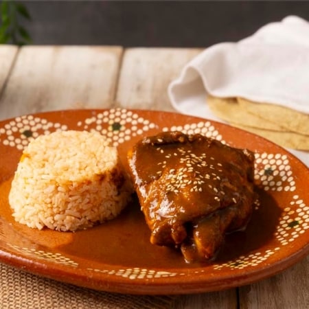 pollo con mole de guayaba y semillas acompañado por arroz sobre plato de cerámica con dibujos, sobre mesa de madera