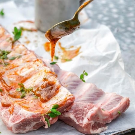 persona preparando costillas de cerdo con mole de guayaba como glaseado para grillar, sobre papel de hornear