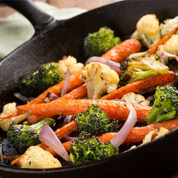 brócoli, coliflor, zanahoria y cebolla morada cortada en sartén de hierro sobre mesa de madera, verduras precocidas