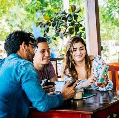 Young friends in a coffee shop with their cell phones having a good time. Three people in a coffee shop with phones having a good time. Three teenage friends on their cell phones in a coffee shop