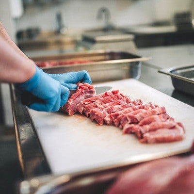 closeup view of a young caucasian man cutting raw pork neck with sharp knife. He makes steaks for grill in restaurant kitchen