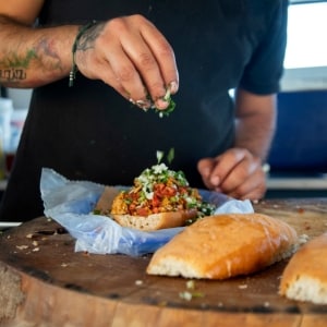 Hombre agrega hierbas frescas a una torta rellena, dejándola lista para envolverla en papel y entregarla al cliente de su remolque de comidas.