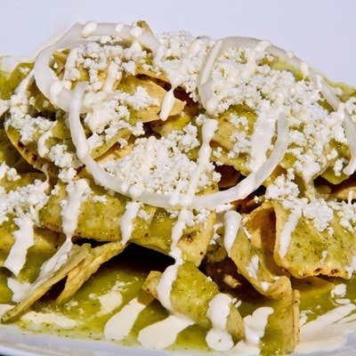 Green Chilaquiles with cheese and sour cream served in a ceramic plate