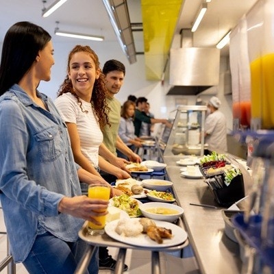 Happy Latin American women eating at a buffet style cafeteria and holding their trays